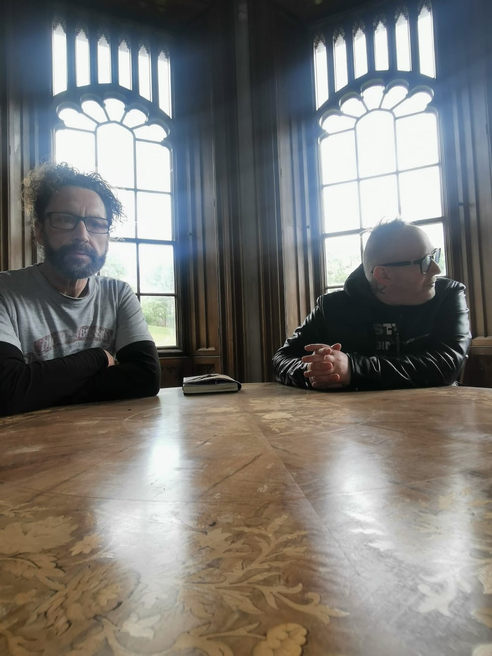 Simon and Kelly sitting at a table with a leather-bound book in castle gothic-style room.