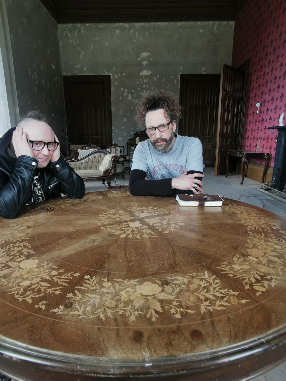 Simon and Kelly sitting at a table with a leather-bound book in castle gothic-style room.
