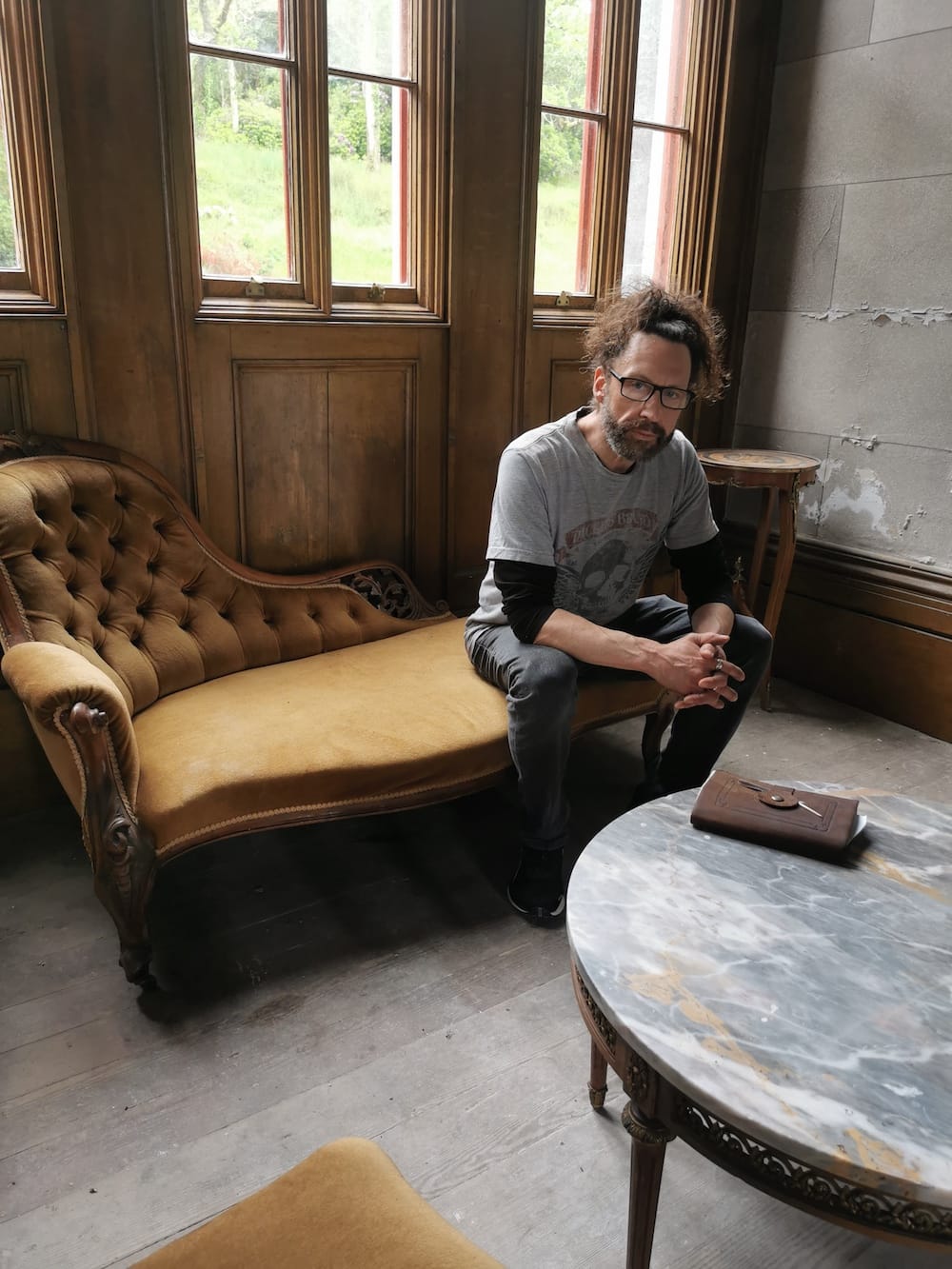 Kelly sits in castle on antique chaise lounge in room with marble table and large windows.