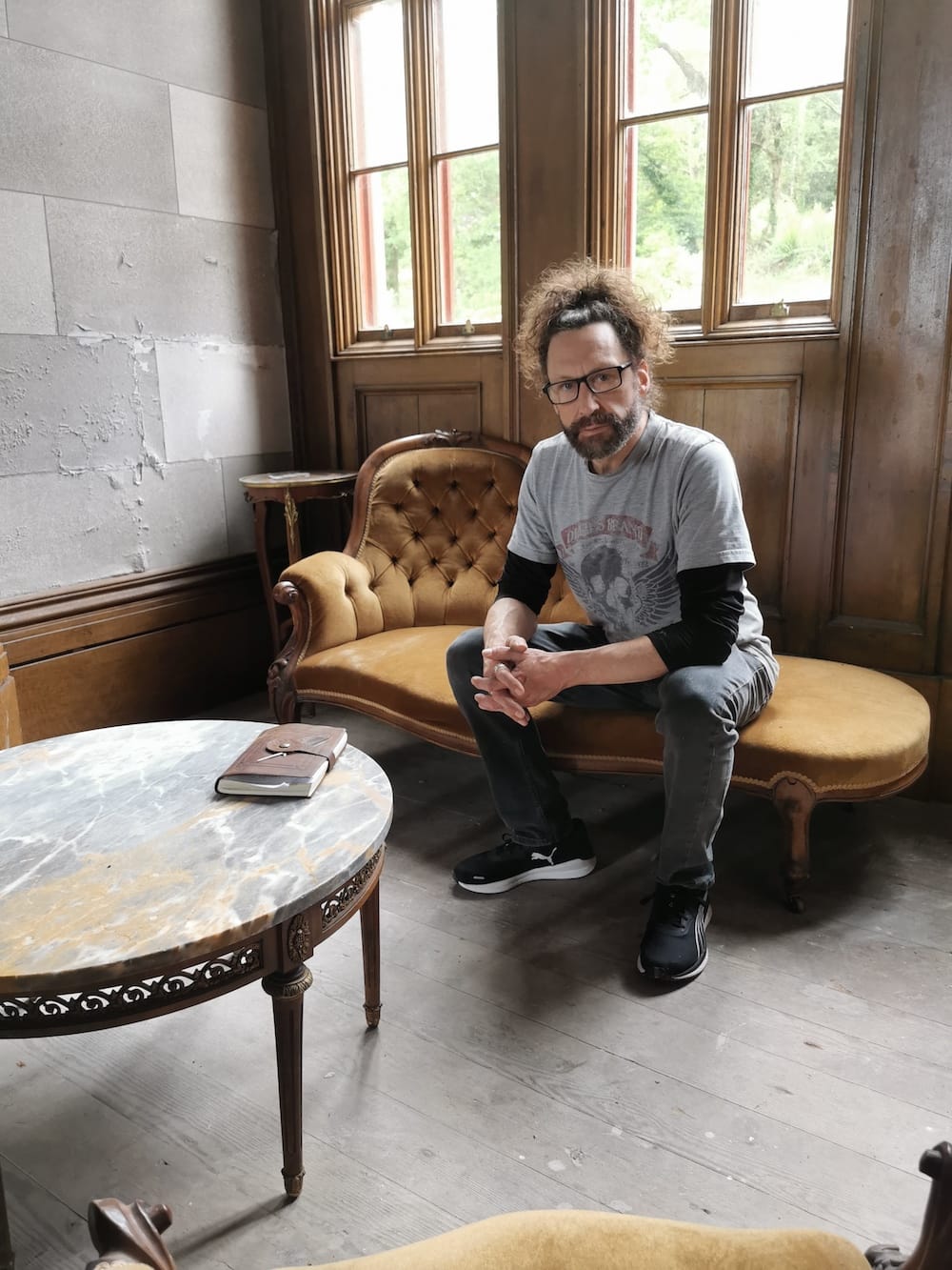 Kelly sits in castle on antique chaise lounge in room with marble table and large windows.